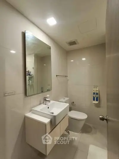 Modern bathroom with sleek fixtures and neutral tones, featuring a wall-mounted sink and large mirror.
