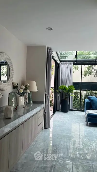 Elegant living room with large windows and modern decor, featuring a lush garden view.
