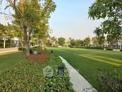 Spacious green garden area in a residential community with lush trees and well-maintained pathways.