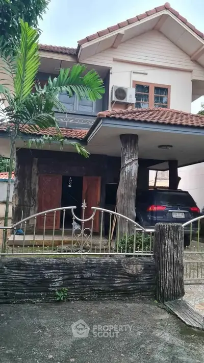Charming two-story house with rustic wooden pillars and a tiled roof, featuring a carport and lush greenery.