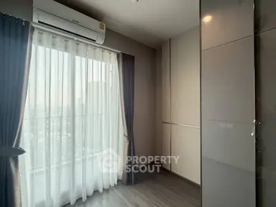 Modern bedroom with large window and sleek air conditioning unit, offering ample natural light.