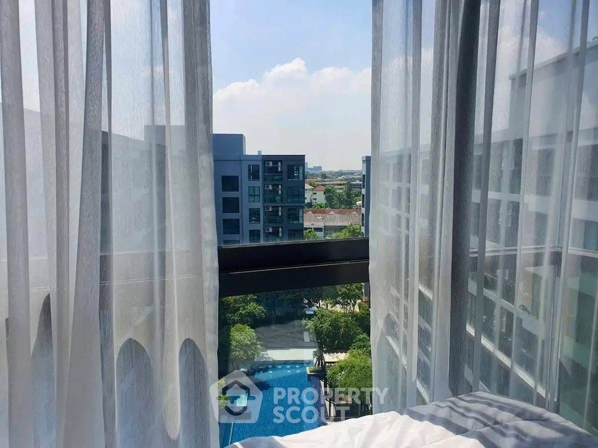 Stunning view from a high-rise apartment overlooking a pool and cityscape, framed by elegant sheer curtains.