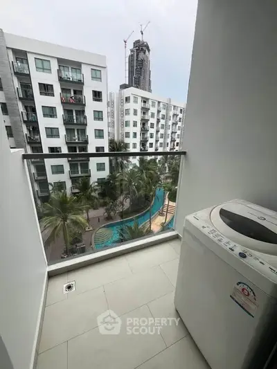 Modern apartment balcony with washing machine and pool view in urban setting.