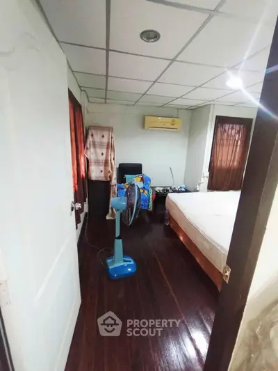 Cozy bedroom with wooden flooring and air conditioning, featuring a comfortable bed and ceiling fan.