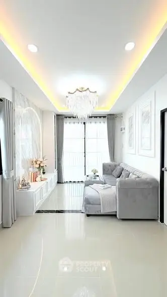 Elegant living room with modern chandelier and cozy gray sofa, featuring large windows and stylish decor.