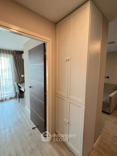 Modern apartment interior with stylish wooden door and built-in storage cabinet, featuring natural light from large window.