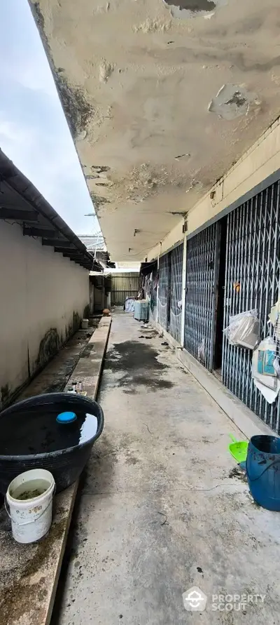 Outdoor corridor with weathered walls and metal gates, showcasing potential for renovation.