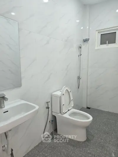 Modern bathroom with sleek white tiles, featuring a toilet, sink, and shower area, offering a clean and minimalist design.