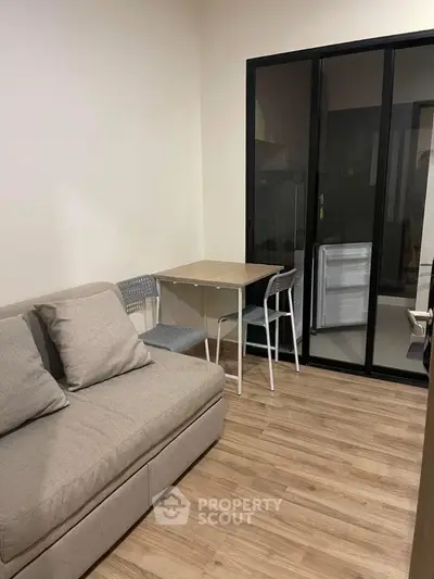 Cozy living room with modern sofa and dining table, featuring sleek wooden flooring and glass partition.
