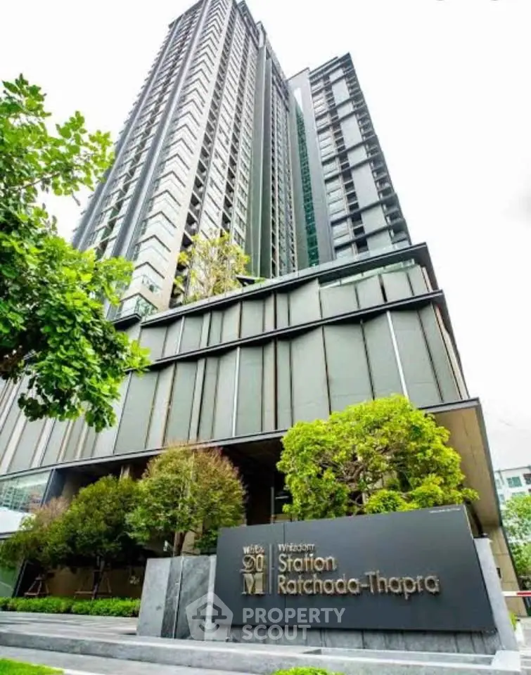 Modern high-rise building with lush greenery at entrance, showcasing urban living.
