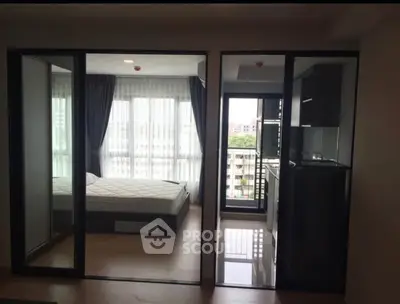 Modern apartment with glass partitions, featuring a bedroom and compact kitchen area.