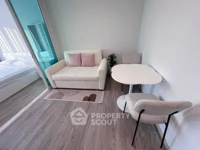 Modern living room with sleek furniture and wooden flooring, adjacent to a cozy bedroom.