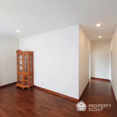 Spacious and well-lit corner unit with polished hardwood floors and a classic wooden display cabinet, perfect for elegant living.