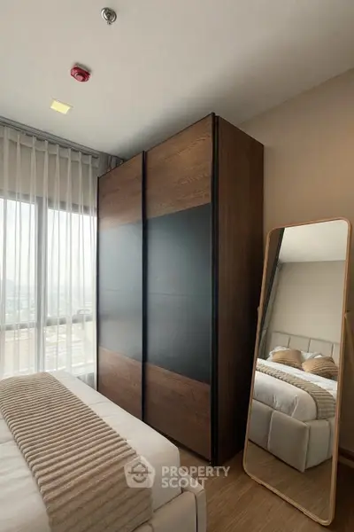 Modern bedroom with stylish wardrobe and full-length mirror, featuring cozy bedding and natural light.