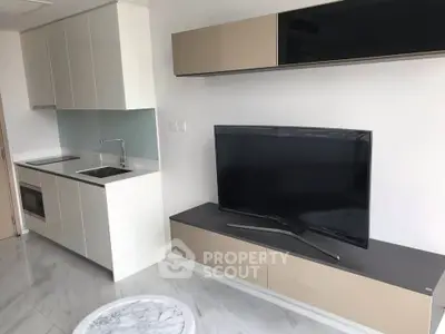 Modern living room with sleek kitchen and flat-screen TV, featuring minimalist design and stylish cabinetry.