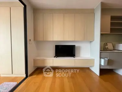 Modern living room with sleek wooden cabinets and mounted TV, adjacent to a compact kitchen area.