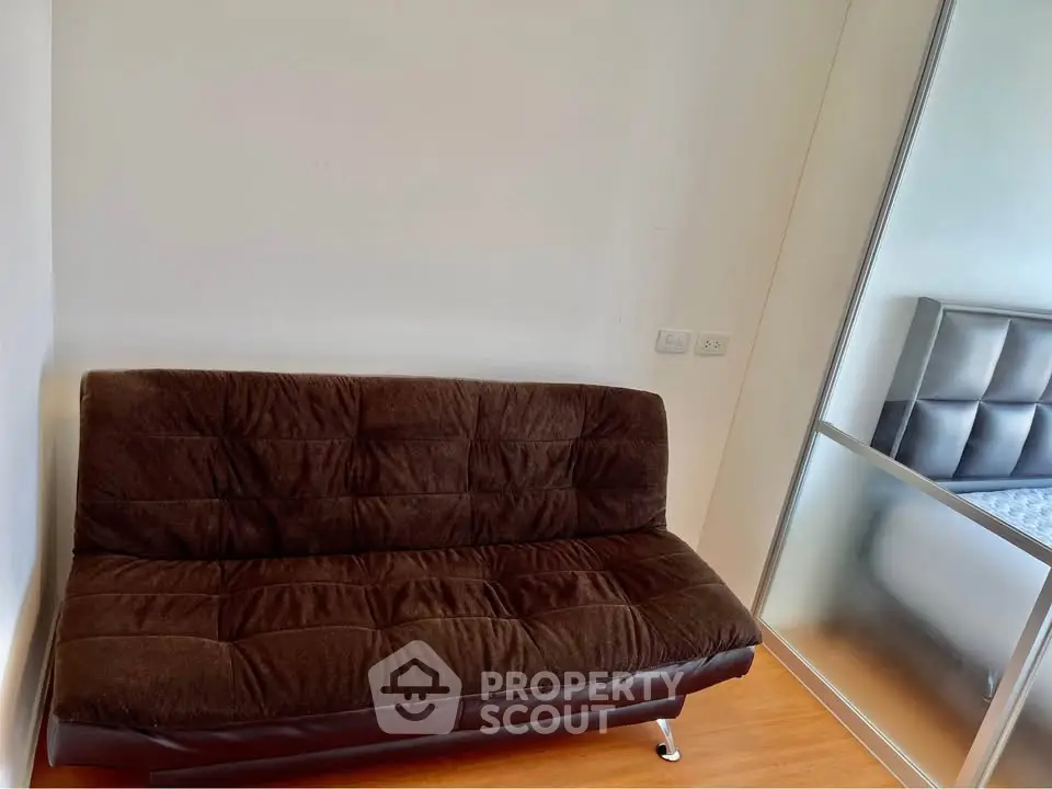 Cozy small living area with brown sofa and mirrored wardrobe, perfect for compact spaces.