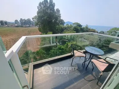 Stunning balcony with glass railing offering panoramic views of lush greenery and distant water.