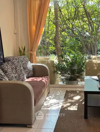 Cozy living room with large window and garden view, featuring a comfortable sofa and stylish decor.