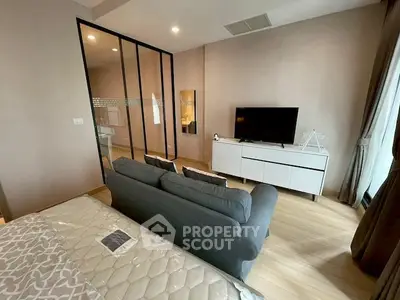 Modern bedroom with cozy seating area and TV, featuring stylish decor and natural light.