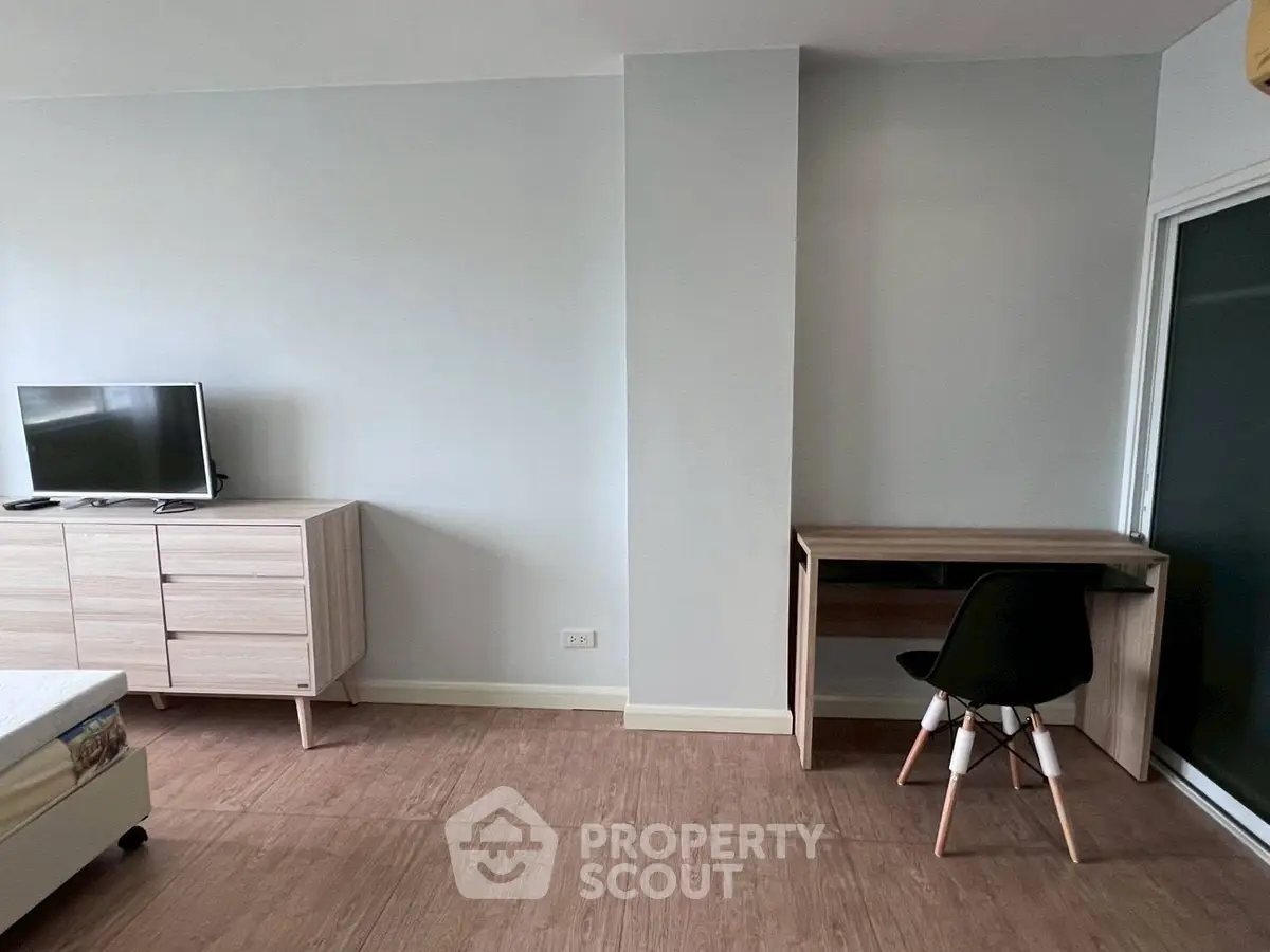 Modern minimalist bedroom with TV, dresser, and study desk in a cozy apartment.