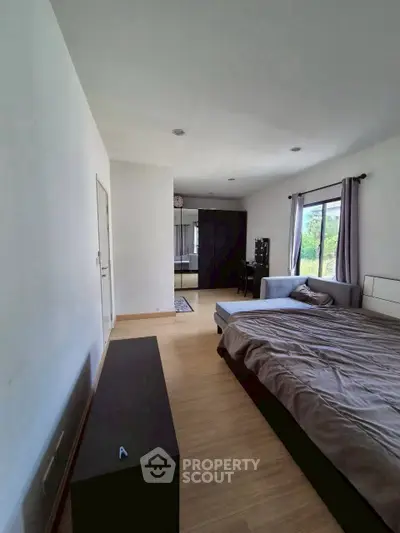 Spacious bedroom with large window and modern decor, offering serene views and ample natural light.