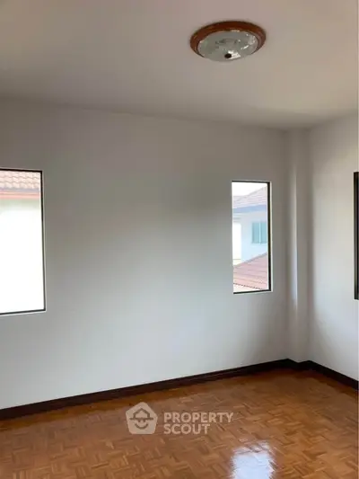 Bright empty room with wooden flooring and two windows, ideal for customization.