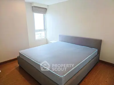 Spacious bedroom with large window and modern bed frame, offering ample natural light and comfort.