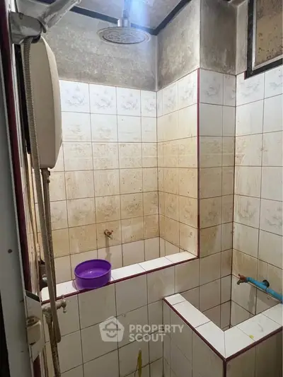 Compact bathroom with tiled walls and ceiling shower, featuring a purple basin and basic fixtures.