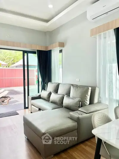 Modern living room with sleek gray sofa and large windows overlooking patio.
