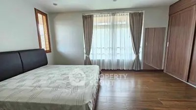 Spacious bedroom with wooden flooring and large window for natural light