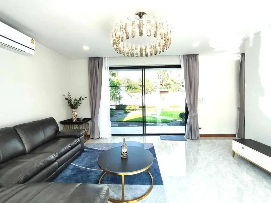 Spacious living room with polished marble floors, elegant chandelier, and large windows leading to a lush garden view, perfect for sophisticated living.