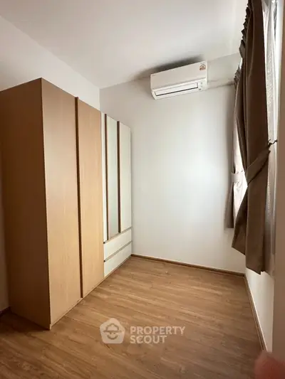 Spacious bedroom with wooden flooring and large wardrobe, featuring natural light from window.