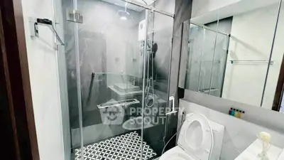 Modern bathroom with glass shower enclosure and stylish black and white tile flooring.