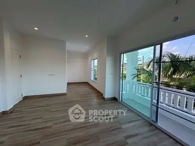 Spacious living room with large windows and balcony access, featuring modern wood flooring and abundant natural light.