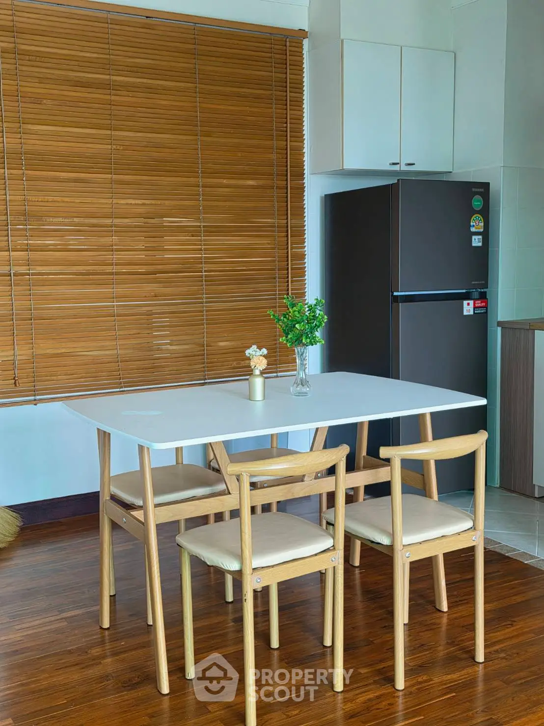 Modern kitchen with wooden flooring, dining table, and sleek refrigerator