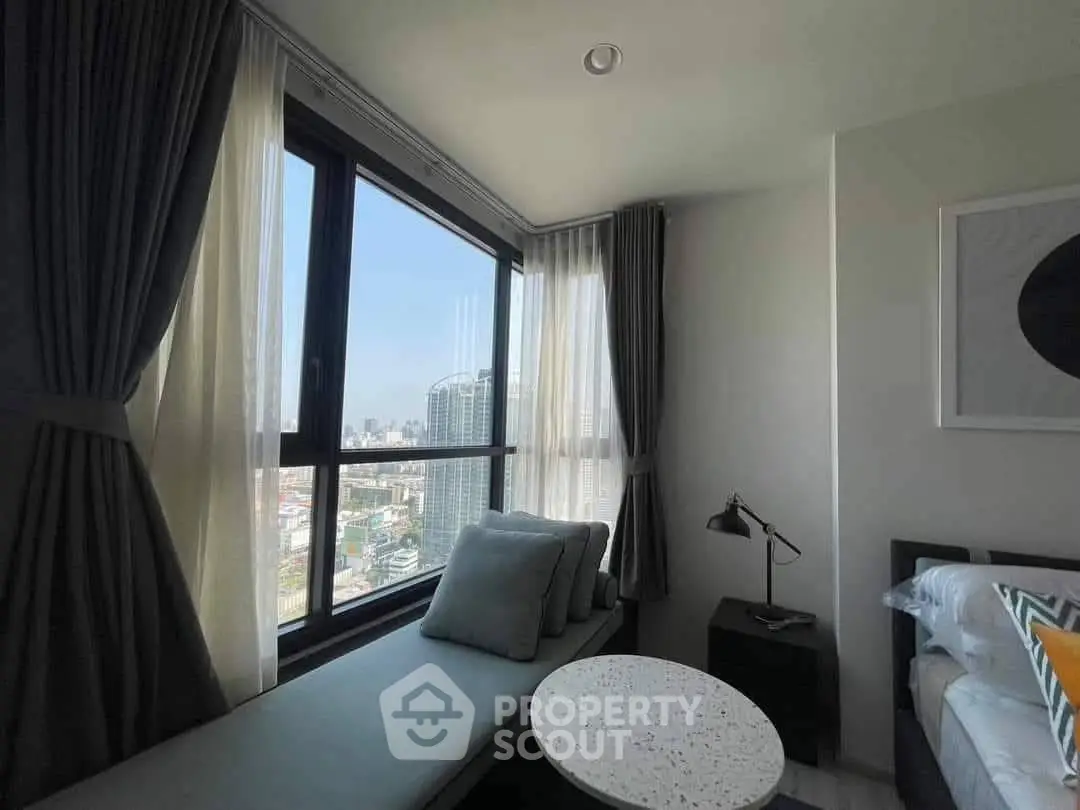 Modern bedroom with large windows offering stunning city views and cozy seating area.