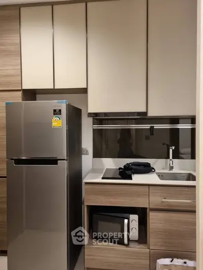 Modern kitchen with sleek cabinets, stainless steel fridge, and built-in microwave in a compact layout.