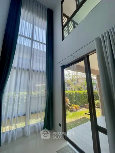 Spacious living room with high ceilings and large windows overlooking a lush garden.
