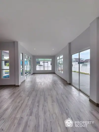 Expansive modern living room with abundant natural light, featuring elegant wood flooring and floor-to-ceiling windows leading to a refreshing outdoor view.