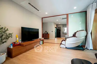 Spacious living room with modern decor and massage chair, featuring wooden flooring and large TV setup.