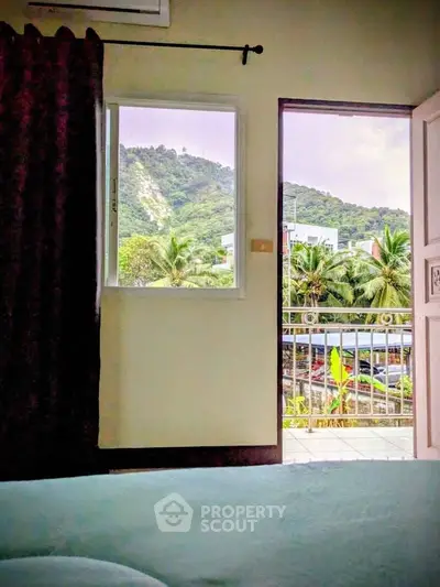 Charming bedroom with balcony offering lush mountain and palm tree views.