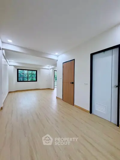 Spacious empty room with wooden flooring and large window, ideal for customization.