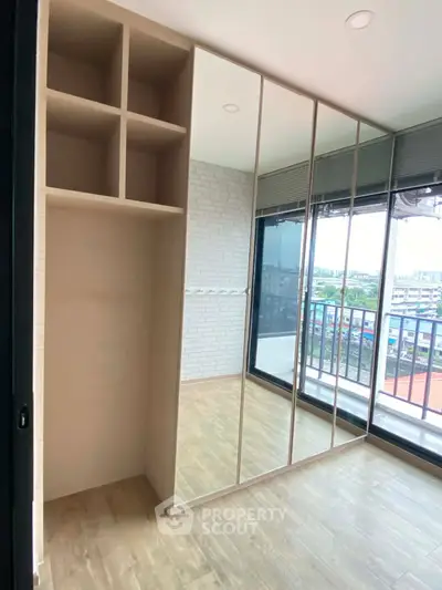 Spacious bedroom with mirrored wardrobe and city view balcony in modern apartment.