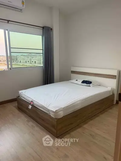 Modern bedroom with wooden flooring and large window offering natural light.