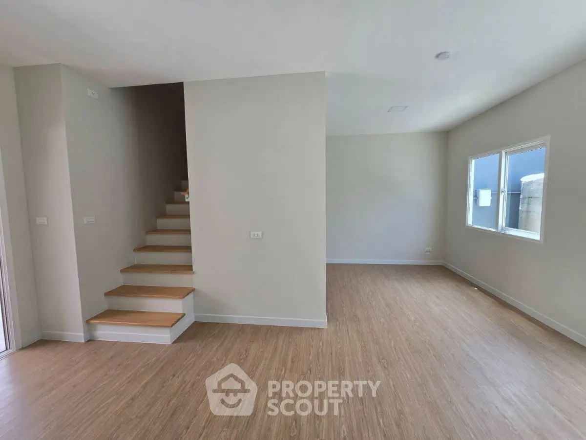 Spacious modern living room with wooden flooring and staircase, ample natural light.