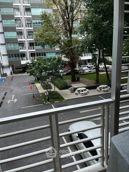 Modern apartment balcony view overlooking parking and garden area.