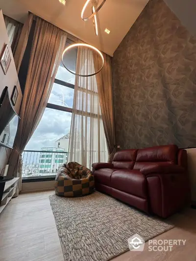 Modern living room with high ceilings and large windows, featuring a red leather sofa and stylish lighting.