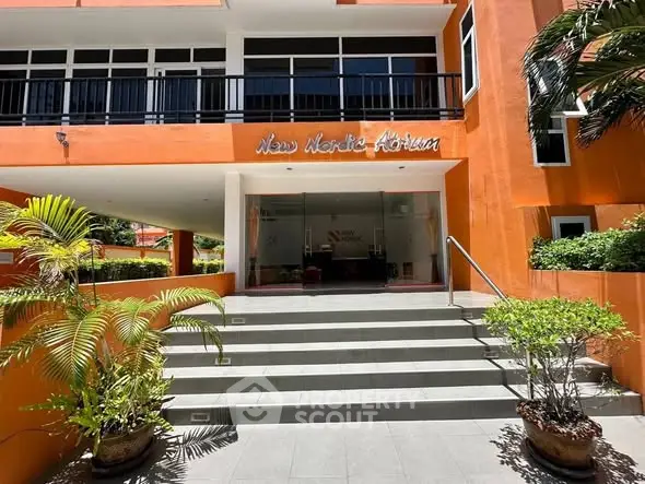 Modern building entrance with vibrant orange facade and lush greenery.