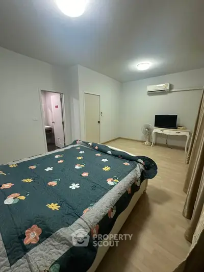Spacious bedroom with floral bedding, air conditioning, and wooden flooring.